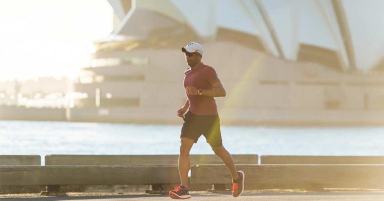 Man running along a harbor with Sydney Opera House in background